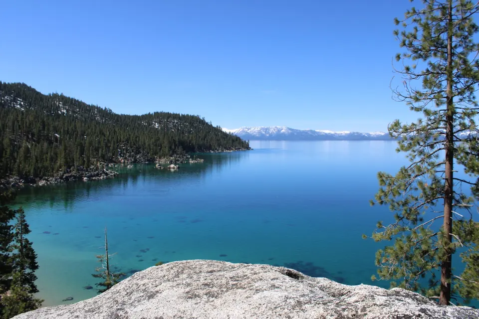 Granite overlook above a calm, clear Lake Tahoe cove with snow-capped peaks across the water